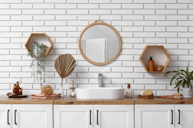 Lavabo, banyo malzemeleri çekmeceler, ayna ve raflar banyodaki beyaz tuğla duvar.