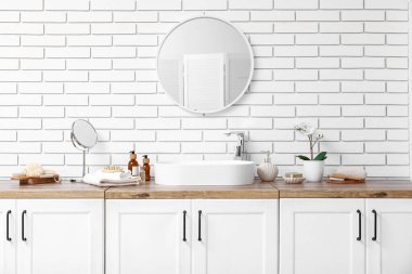 Lavabo, çekmecelerde kozmetik ürünleri ve banyoda beyaz tuğla duvarlarda ayna.