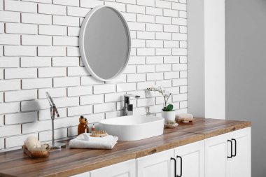 Lavabo, çekmecelerde kozmetik ürünleri ve banyoda beyaz tuğla duvarlarda ayna.