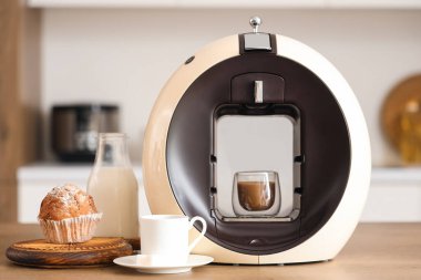 Mutfaktaki masada kapuçino ve kek ile modern kahve makinesi.