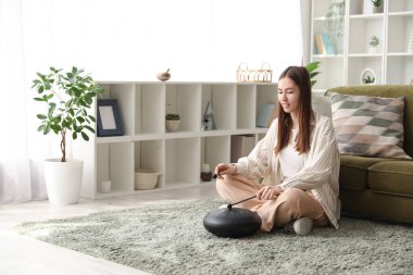 Evde halıda glukofon çalan genç bir kadın.