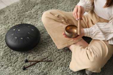 Tibet şarkı kasesi olan genç bir kadın evdeki halıda oturuyor, yakın plan.