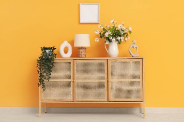 Çekmeceli güzel bir oda, lamba ve çiçek açan ağaç dalları turuncu duvarın yanında.