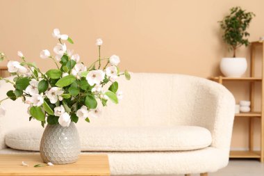 Kahve masası, yumuşak kanepe ve çiçek açan ağaç dalları olan şık bir oturma odası.