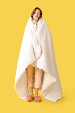 Sarı arka planda esneyen battaniyeli güzel genç bir kadın.
