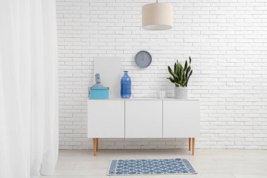 Dekoratif şişe, ev bitkisi ve heykelcik beyaz tuğla duvarın yanındaki modern dolapta.