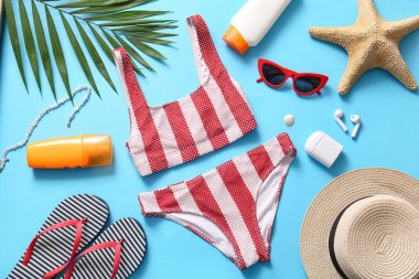 Mavi arka planda plaj aksesuarları, mayo ve güneş kremi.