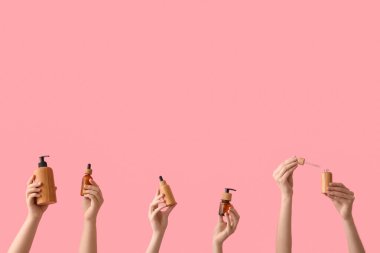 Kadın elleri ve pembe arka planda kozmetik ürünleri şişeleri ve pipetleri.
