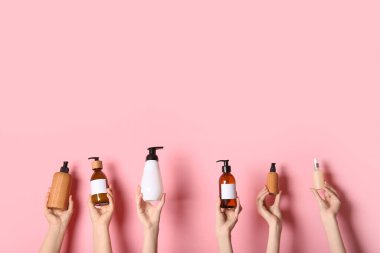 Pembe arka planda farklı kozmetik ürünleri şişeleri olan kadın elleri