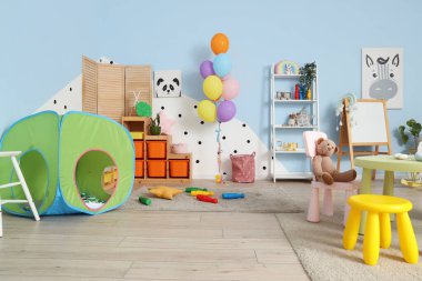Anaokulundaki modern oyun odasının içinde oyun çadırı ve sandalyeli bir masa var.