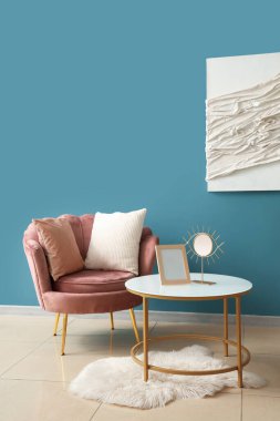 Yastıklı koltuk, aynalı sehpa ve oturma odasındaki resimli mavi duvarın yanındaki çerçeve.