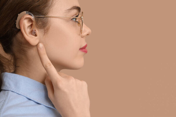 Красивая молодая женщина указывает на слуховой аппарат на коричневом фоне