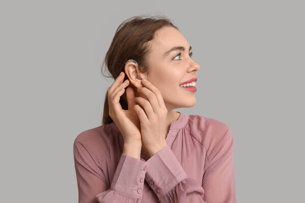 Счастливая молодая женщина со слуховым аппаратом на сером фоне