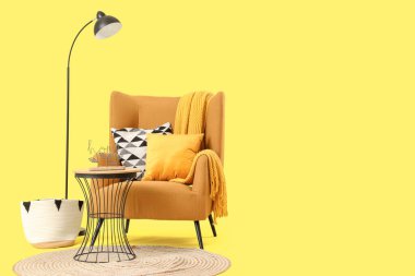 Koltuk, yastık, ekose, lamba ve kahve sehpası sarı arka planda.