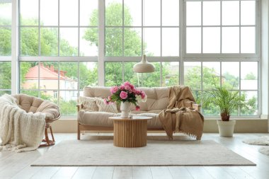 Kahve masasının üstünde, kanepenin yanında ve oturma odasındaki koltuğun yanında güzel şakayık çiçekleri olan vazo.