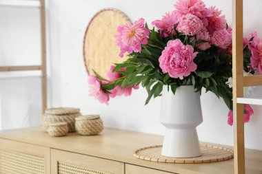 Hasır kutuların yanında pembe şakayık çiçekleri vazosu oturma odasındaki çekmecelerin üstünde.