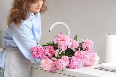 Mutfakta elinde bir buket güzel şakayık çiçeğiyle genç bir kadın.