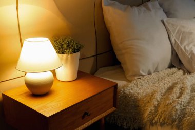 Yatak odasının içinde parlayan lamba olan komodinin yanında.