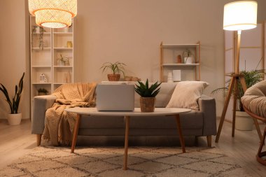 Kanepesi, koltuğu, laptoplu sehpası ve parlak lambaları olan şık bir oturma odası.