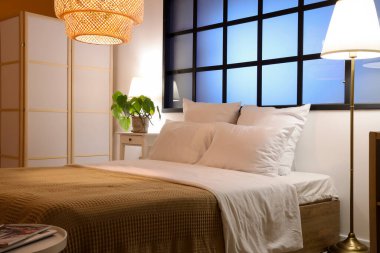 Yatak odasının içinde rahat bir yatak odası, komodin ve parlayan lambalar.