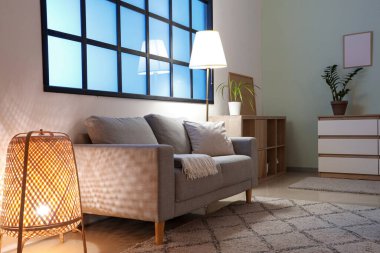 Kanepe, çekmeceler, ev bitkileri ve oturma odasının içinde parlayan lambalar.