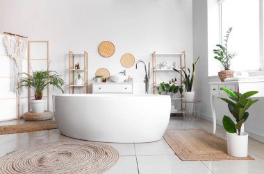 Interior of light bathroom with bathtub and houseplants