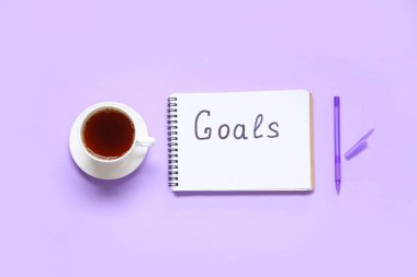 Metin hedefli defter, bir fincan çay ve leylak arkaplanlı kalem