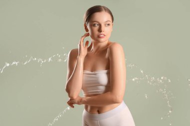 Gri arka planda su damlatan güzel genç bir kadın.