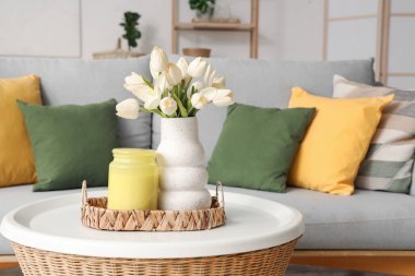 Kavanozlu hasır tepsi ve vazodaki çiçekler oturma odasındaki yuvarlak masada.