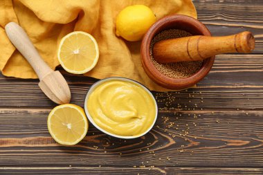 Kahverengi ahşap arka planda bir kase kremalı hardal ve limon.
