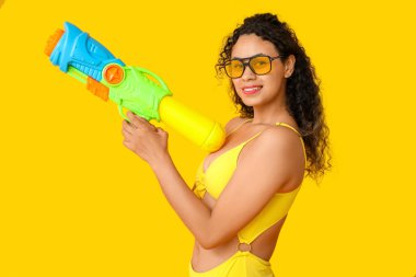 Sarı arka planda su tabancası olan mutlu Afro-Amerikalı kadın.