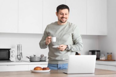 Dizüstü bilgisayarı ve kahvesi olan genç bir erkek öğretmen evde online ders veriyor.