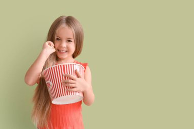 Yeşil arka planda patlamış mısır dolu küçük mutlu bir kız.