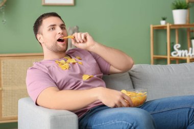 Evdeki kanepede oturan bir kase patates cipsiyle yakışıklı genç adam.