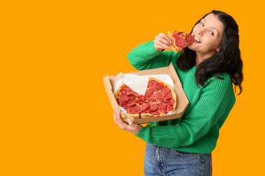 Güzel genç bir kadın sarı arka planda lezzetli pizzalar yiyor.