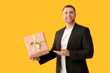 Yakışıklı genç adam sarı arka plandaki hediye kutusunu işaret ediyor.