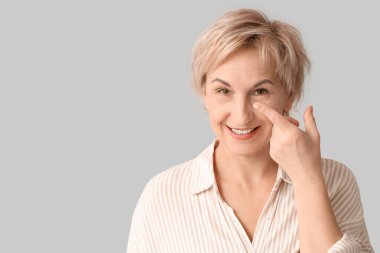 Gri arka plana kontak lens takan olgun bir kadın