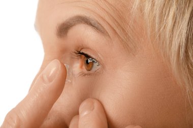 Olgun kadın beyaz arka plana kontak lens takıyor, yakın plan.