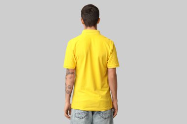 Gri arka planda, şık sarı tişörtlü yakışıklı genç adam.