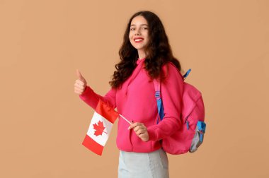 Kanada bayrağı ve sırt çantasında kahverengi arka planda baş parmak hareketi gösteren bir bayan öğrenci.