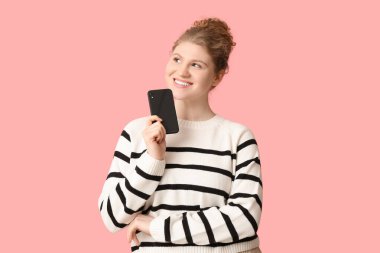Pembe arka planda cep telefonu olan mutlu, güzel bir kadın.