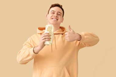 Genç mutlu adam gülümsüyor ve bej arka planda lezzetli bir donör kebabı tutuyor.