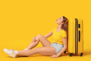 Sarı valizli güzel genç bir kadın, arka planda oturuyor.