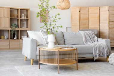 Şık oturma odasının içinde rahat bir kanepe, sehpa ve vazoda çiçek açan ağaç dalları var.