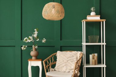 Yeşil oturma odasındaki rahat koltuğun yanındaki sehpanın üzerinde çiçek açan bir vazo.