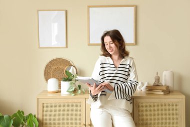 Şarjörü olan genç bir kadın, evdeki bej duvarlara boş çerçeveler asıyor.