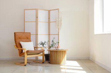 Koltuğu, masası ve katlanır ekranı olan aydınlık oturma odasının içi