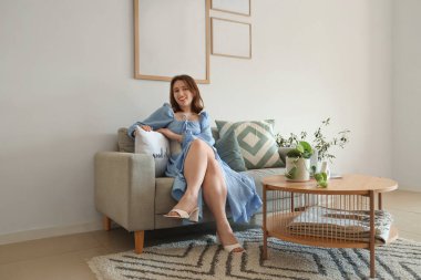 Kanepede oturan genç bir kadın. Evinde boş kareler asıyor.