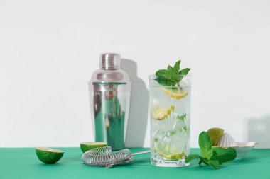 Beyaz arka planda yeşil masada kokteyl süzgeci ile bir bardak taze mojito.