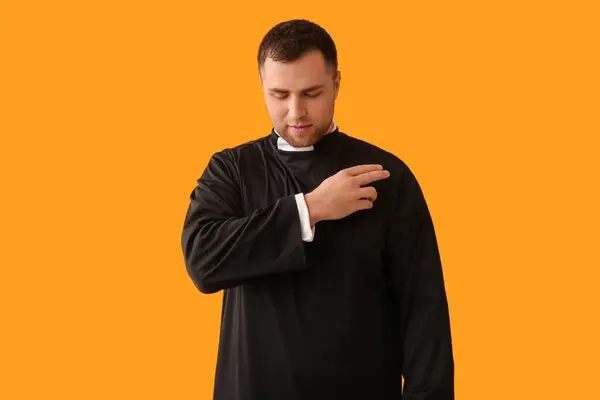 stock image Young priest cross oneself on yellow background